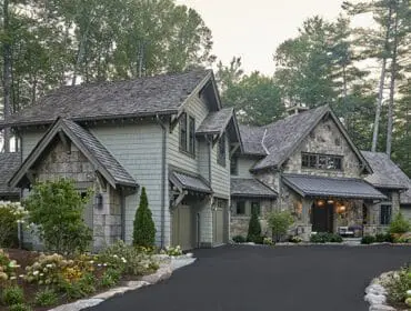 Stone and shingle house with dark metal roof and manicured landscaping