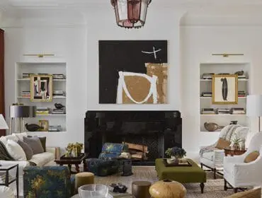 Living room with white sofas, patterned armchairs, a black marble fireplace with abstract art above, and built-in bookshelves flanking the fireplace.