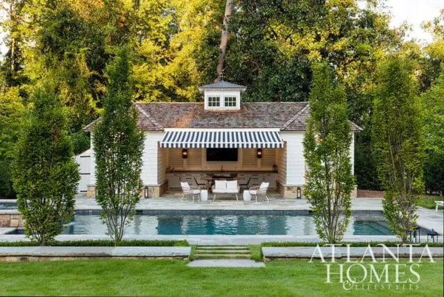 Outdoor living space with a pool and covered bar area featuring white shiplap siding, a striped awning, and seating.