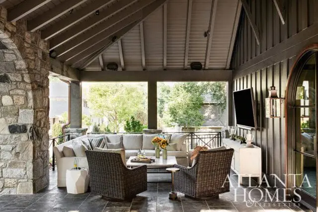 Covered patio with stone fireplace, sectional sofa, wicker chairs, and a television mounted on a paneled wall.