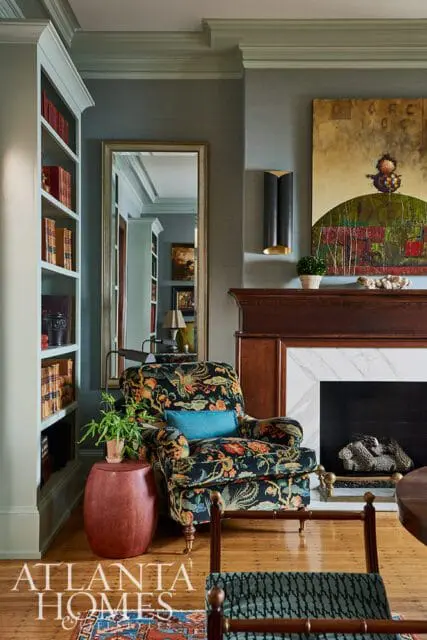 Living room with a patterned armchair, built-in bookshelves, a fireplace with a marble surround, and a large mirror reflecting the room.