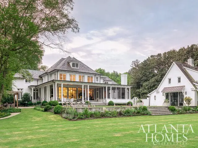 Large white brick house with a screened-in porch and multiple windows, set on a green lawn with mature trees and landscaping.