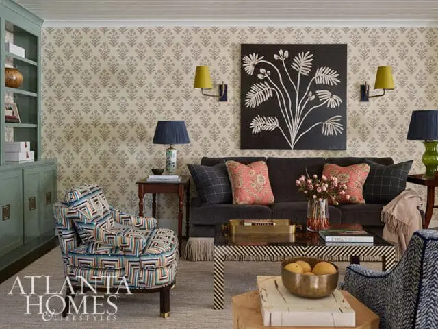 Living room with patterned wallpaper, a dark gray sofa with coral and plaid pillows, a colorful armchair, and a black and white striped coffee table.