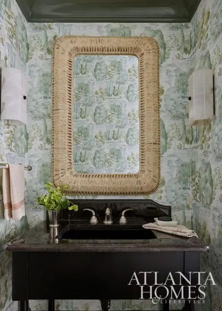 Powder room with scenic toile wallpaper, a black granite vanity with a silver sink and faucet, and a rectangular mirror with a woven rope frame.