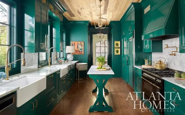 Emerald green high-gloss kitchen with white farmhouse sinks, brass faucets, marble countertops, and a wood-plank ceiling.