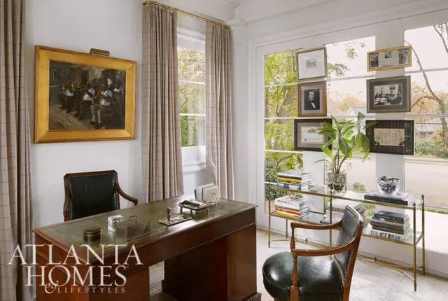 Office with a dark wood desk with green leather inlay, leather chairs, framed artwork, and a gold-framed painting of musicians on the wall.
