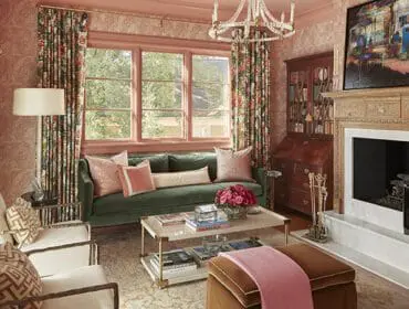 Living room with pink patterned wallpaper, green velvet sofa, ornate fireplace, grand piano, and floral curtains.