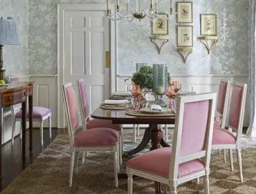 Dining room with light blue floral wallpaper, a dark wood dining table set with pink chairs, and a console table with lamps.