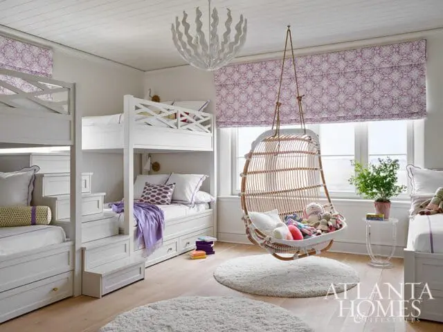 White children's bedroom with bunk beds, a hanging rattan chair, and purple patterned window treatments.