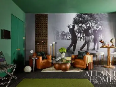 Living room with green walls, a large black and white mural of golfers, leather armchairs, a glass coffee table, and a bar area with stools.