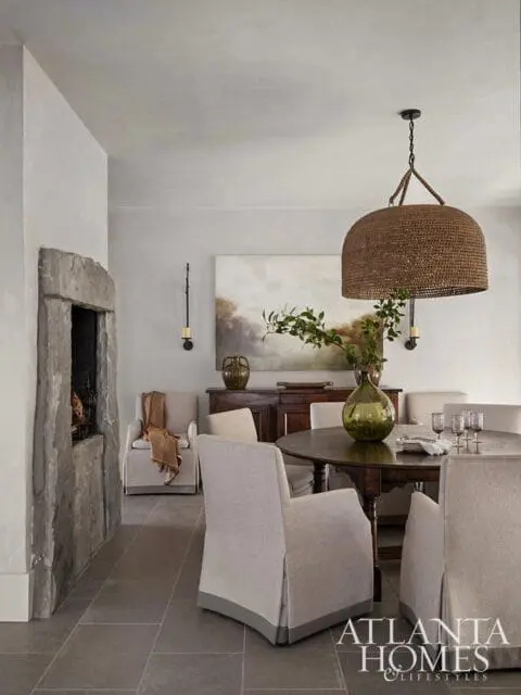 Dining room with a rustic stone fireplace, slipcovered chairs around a dark wood table, and a woven pendant light.