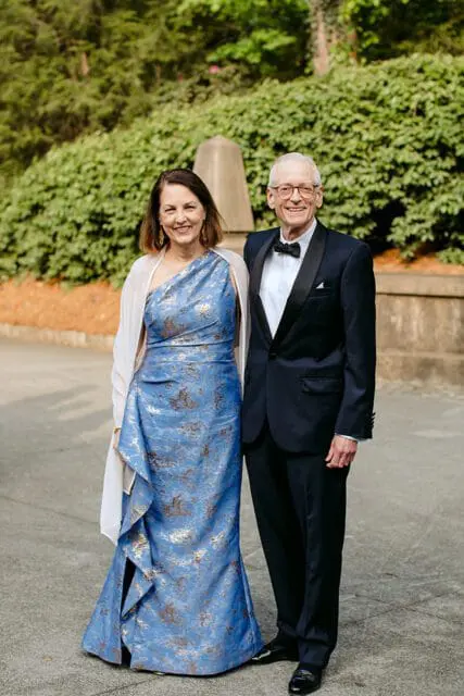 Couple posing outdoors, woman in a blue patterned gown and white shawl, man in a tuxedo.