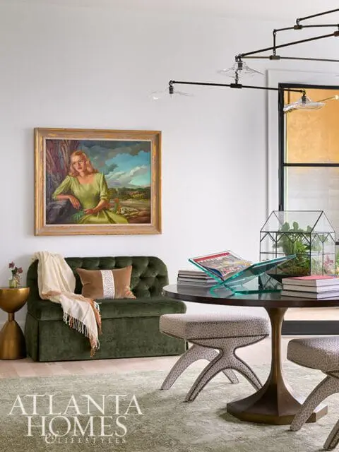 Green tufted sofa with a throw blanket and decorative pillow, next to a round dark wood table with stools and a glass terrarium.