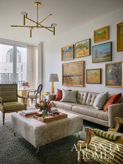 Living room with a tufted leather sofa, patterned armchairs, a cowhide ottoman, and a gallery wall of landscape paintings.