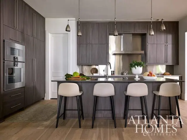 Modern kitchen with dark wood cabinetry, stainless steel appliances, a dark island with four cream bar stools, and pendant lighting.