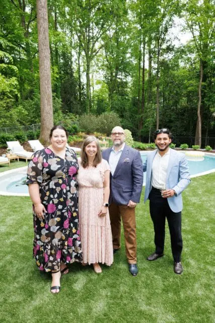 Two women and two men posing for a photo in a backyard with a pool and lounge chairs.