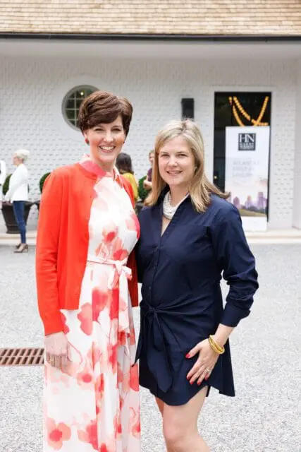 Two women smiling in front of a white building with a sign that reads "HN ATLANTA'S FIRST IN LUXURY"