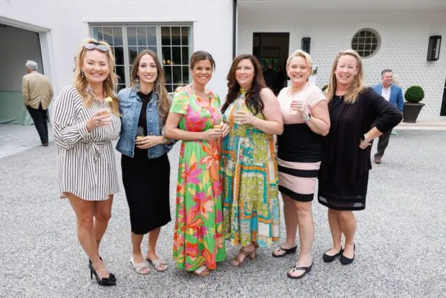 Six women posing for a photo outside a white brick building.