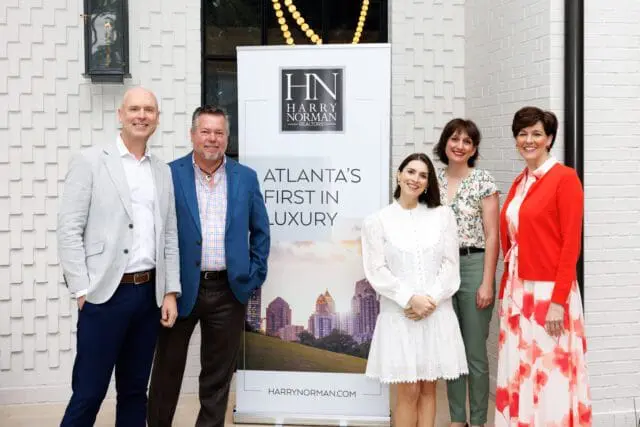 Five people stand in front of a banner with the Harry Norman Realtors logo and the text "Atlanta's First in Luxury."