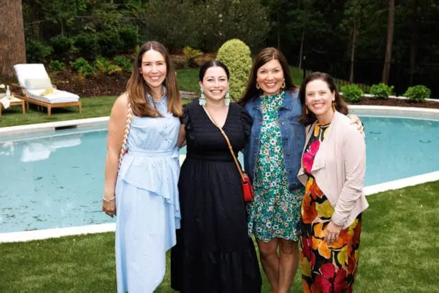 Four women smile for a photo in a backyard setting next to a swimming pool.