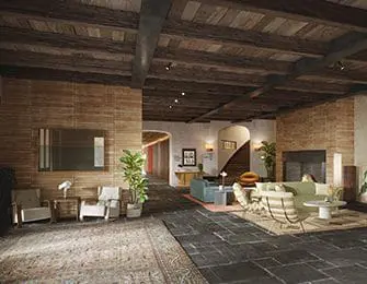 Lobby with dark wood beamed ceiling, brick and wood paneled walls, dark stone tile floor, and seating areas with sofas, chairs, and rugs.