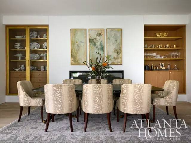 Dining room with a dark wood table surrounded by upholstered chairs with a light-colored animal print. Features built-in wood cabinetry with glass doors displaying dishes and a bar area with glassware.
