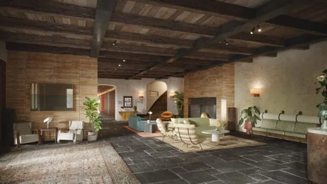 Lobby with dark stone floors, exposed wooden beams, brick walls, and textured plaster walls. Furnishings include green sofas, armchairs, and a fireplace.