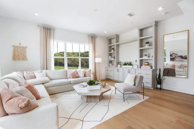 Light-colored sectional sofa with blush pink pillows in a modern living room with a hexagonal coffee table and built-in gray cabinets.