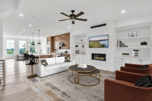 Open-concept living and dining area with white sofa, two rust-colored armchairs, a fireplace, and a kitchen with wood cabinetry and a large island.
