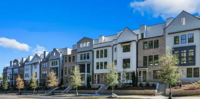 Row of modern townhouses with mixed materials including white siding, gray brick, and dark trim, under a bright blue sky with scattered clouds.