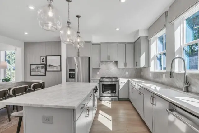 Gray kitchen with marble island and countertops, stainless steel appliances, and glass pendant lights.