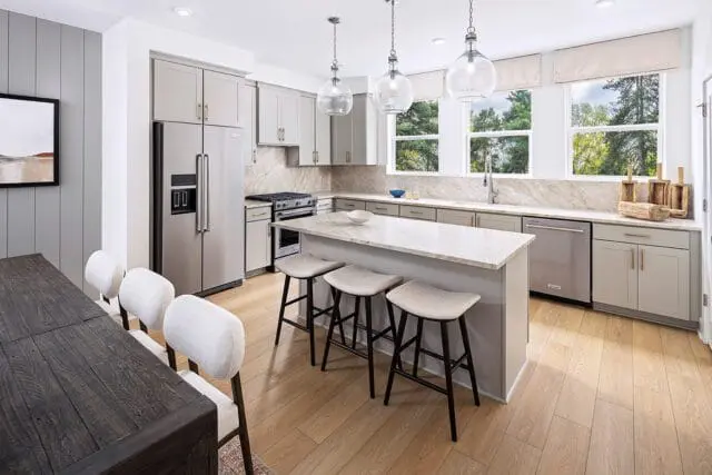 Modern gray kitchen with stainless steel refrigerator, marble island with bar stools, and light wood flooring.