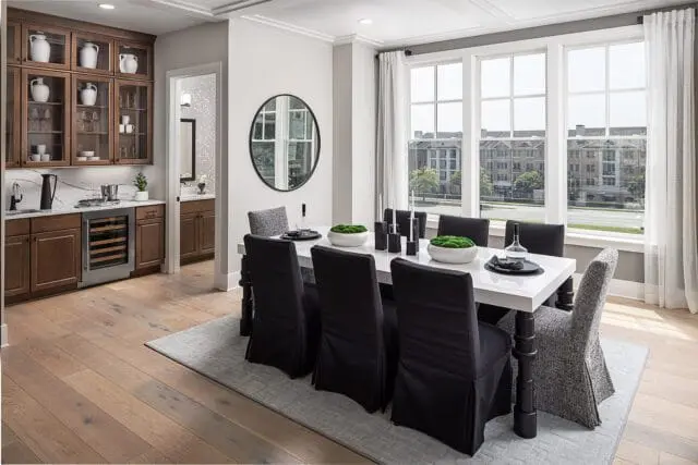 Dining room with white table, black slipcovered chairs, and a built-in bar with glass-front cabinets and a wine fridge.