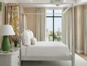 Four-poster bed with beige curtains and city view.