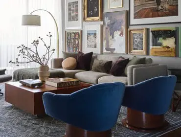 Living room with a sectional sofa, Eames lounge chair, blue velvet chairs, a wooden coffee table, and a gallery wall of artwork.