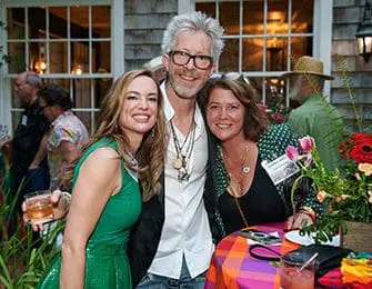 Three people pose for a photo at an outdoor event. A woman in a green dress smiles at the camera, flanked by two people.