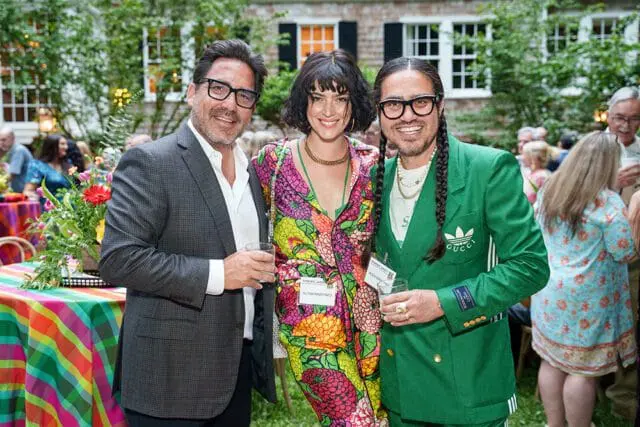 Three people at a garden party, holding drinks.