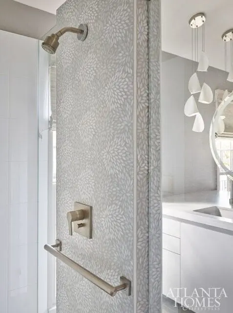 Modern bathroom with a shower featuring white subway tile and a decorative floral mosaic accent wall. Brushed nickel fixtures and a minimalist vanity are visible.