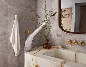 Gray textured walls in a bathroom with a marble vanity, brass fixtures, and a curved architectural detail.
