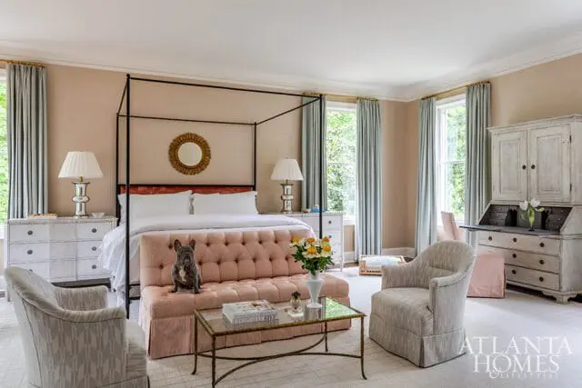 Bedroom with a four-poster bed, tufted pink sofa, French bulldog, antique secretary desk, and light blue curtains.
