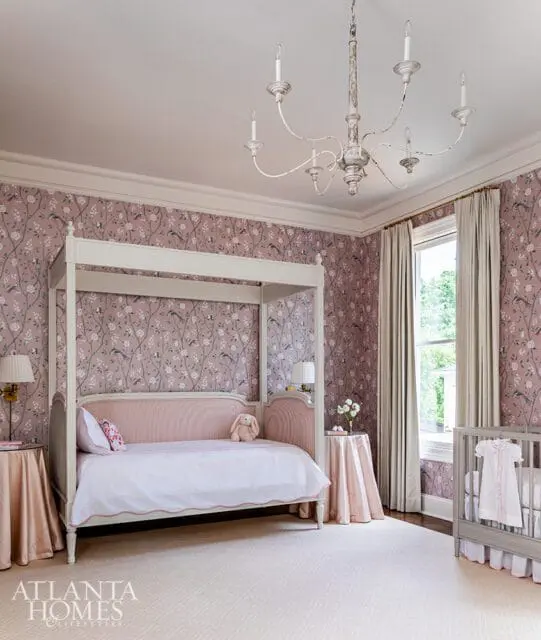 Nursery with a four-poster daybed, pink floral wallpaper, a crib with a white dress, and a distressed white chandelier.