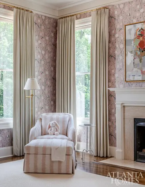 Living room with floral wallpaper, upholstered armchair and ottoman with striped fabric, floor lamp, fireplace, and abstract art above the mantel.