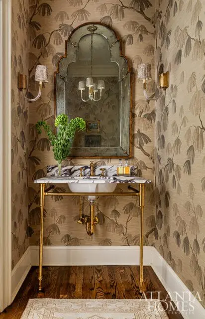 Powder room with botanical wallpaper, a marble-topped console sink with brass fixtures, an ornate mirror, and gold sconces.
