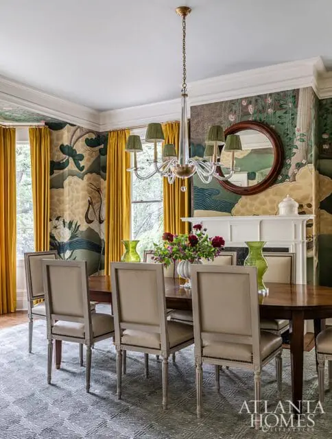 Dining room with a dark wood table and upholstered chairs, a fireplace with a round mirror above, and bold floral wallpaper.