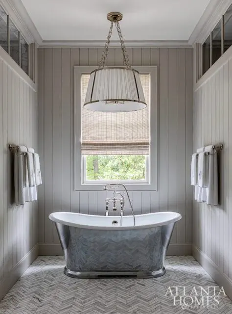 Gray paneled bathroom with a freestanding clawfoot tub featuring a metallic herringbone pattern, a large pleated drum pendant light, and a herringbone tile floor.
