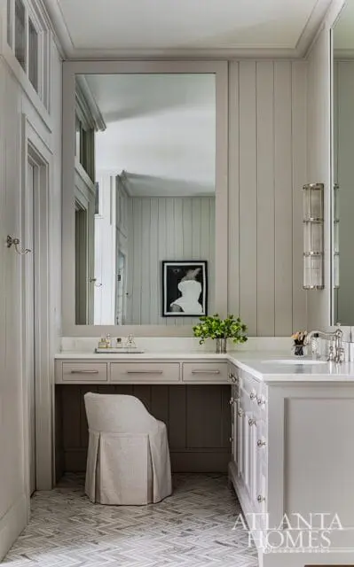 Neutral toned vanity area with a large mirror reflecting paneled walls, a vanity stool, and a marble countertop with a sink and faucet.