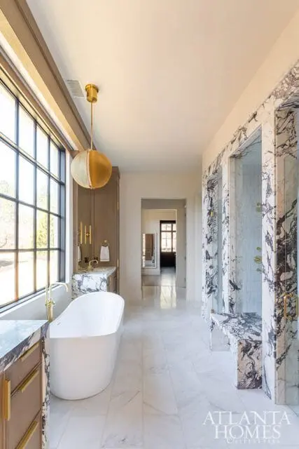 Spacious bathroom with a freestanding white tub, marble-clad shower stalls with glass doors, and a vanity with marble countertop and wood cabinetry.