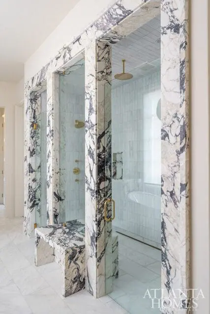 Luxury bathroom with a marble-clad shower enclosure featuring a built-in bench, brass fixtures, and vertical tile walls.