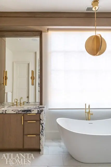 Modern bathroom with a freestanding white bathtub, marble vanity with wood cabinetry and brass fixtures, and a large spherical brass pendant light.