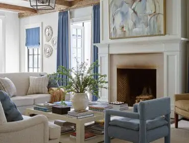 Living room with a cream sofa, blue armchair, and two tan wingback chairs. A white fireplace with a large abstract painting above it is visible.